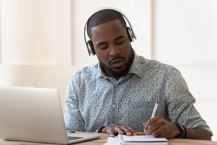 student with computer and notepad wearing headphones