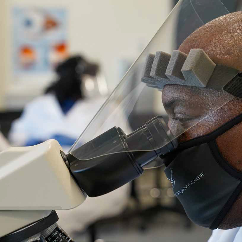student wearing protective equipment looking through a microscope