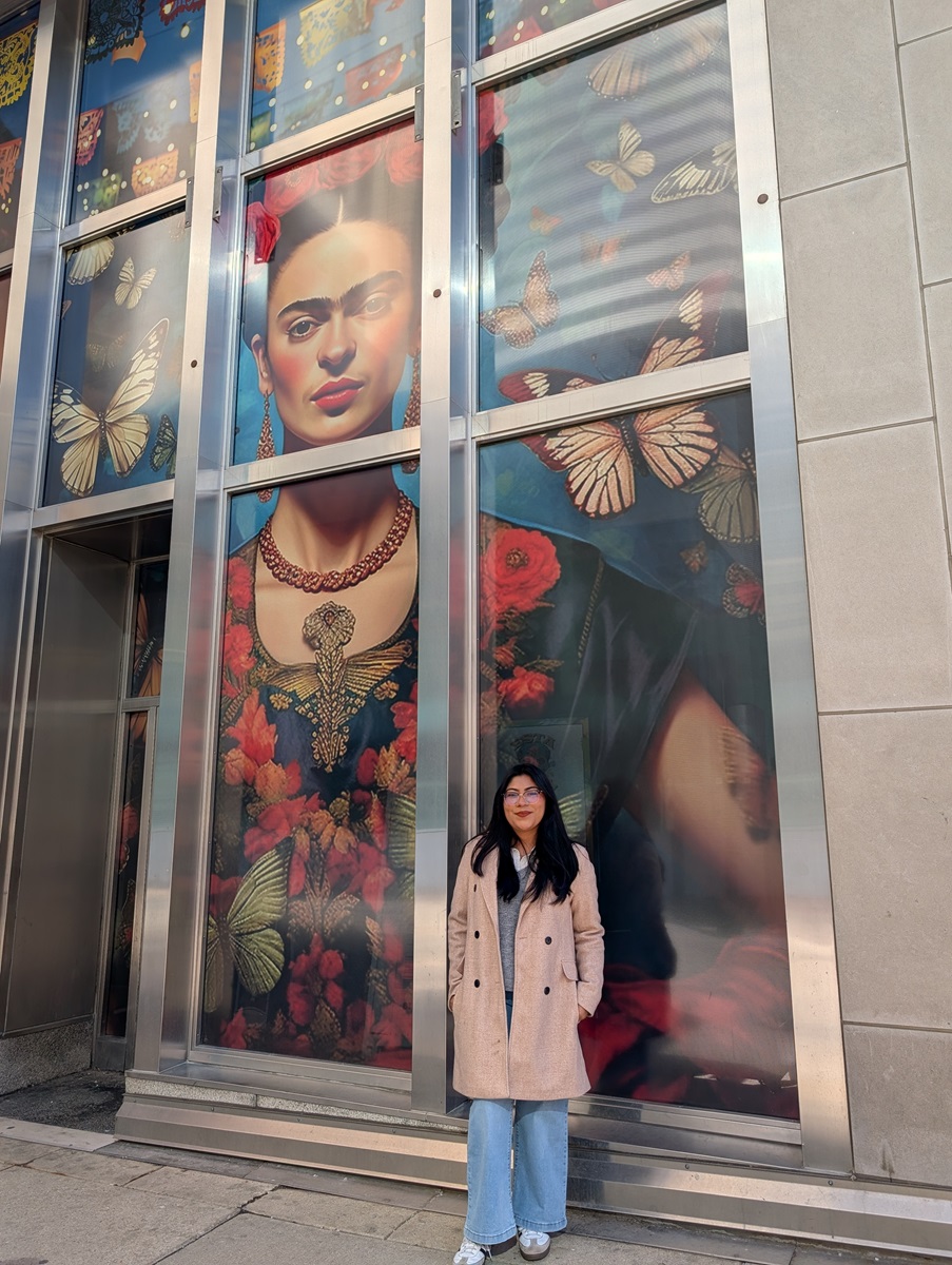 Leslie Arias stands in front of a mural depicting Frida Kahlo