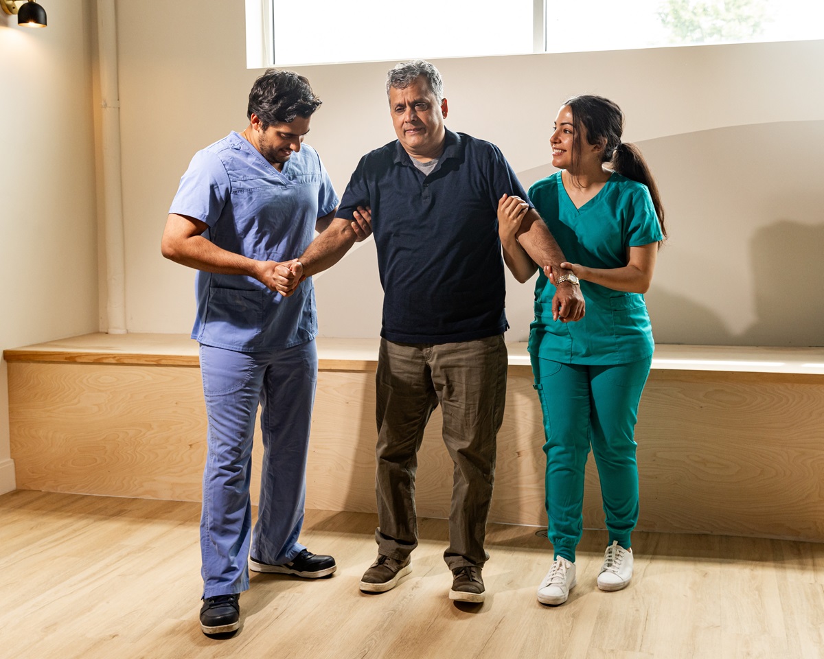 nursing assistants helping a man walk in physical therapy