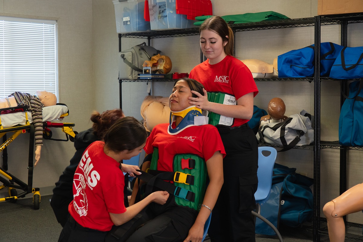 EMT students wrapping a student in emergency medical equipment for training.